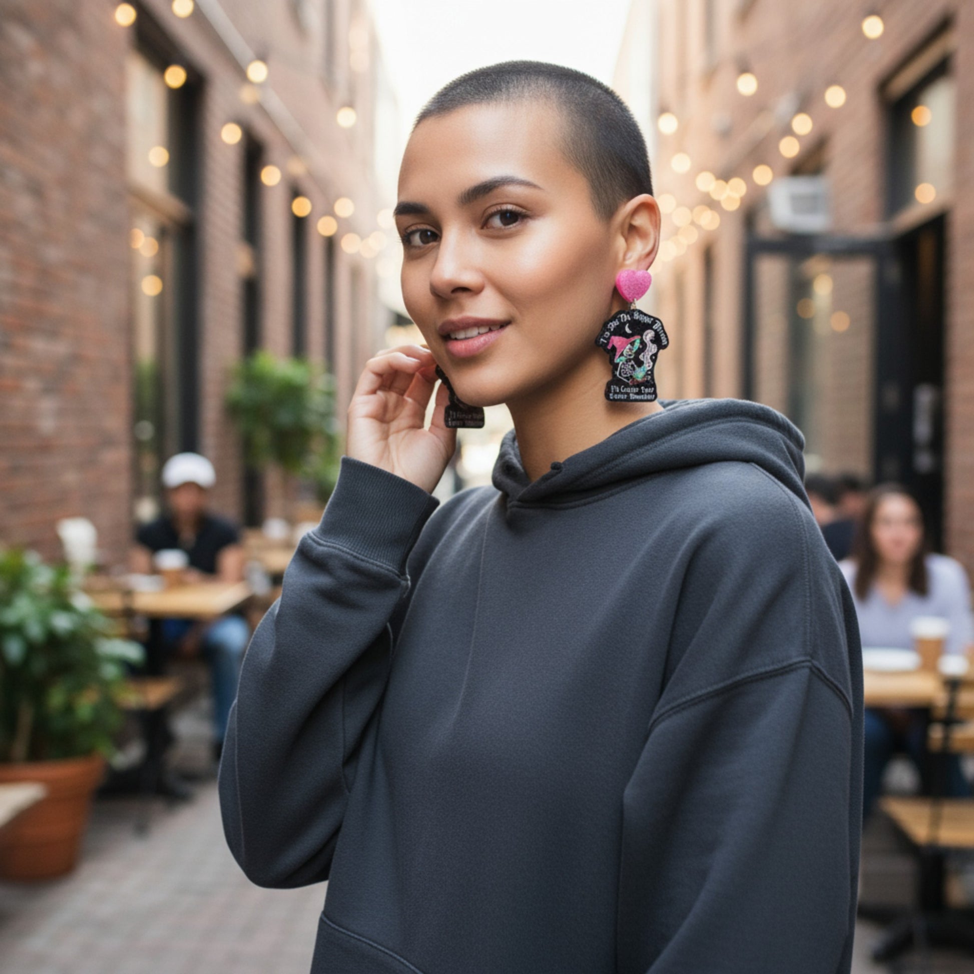 Woman wearing a dark gray hoodie with colorful earrings in an outdoor setting.
