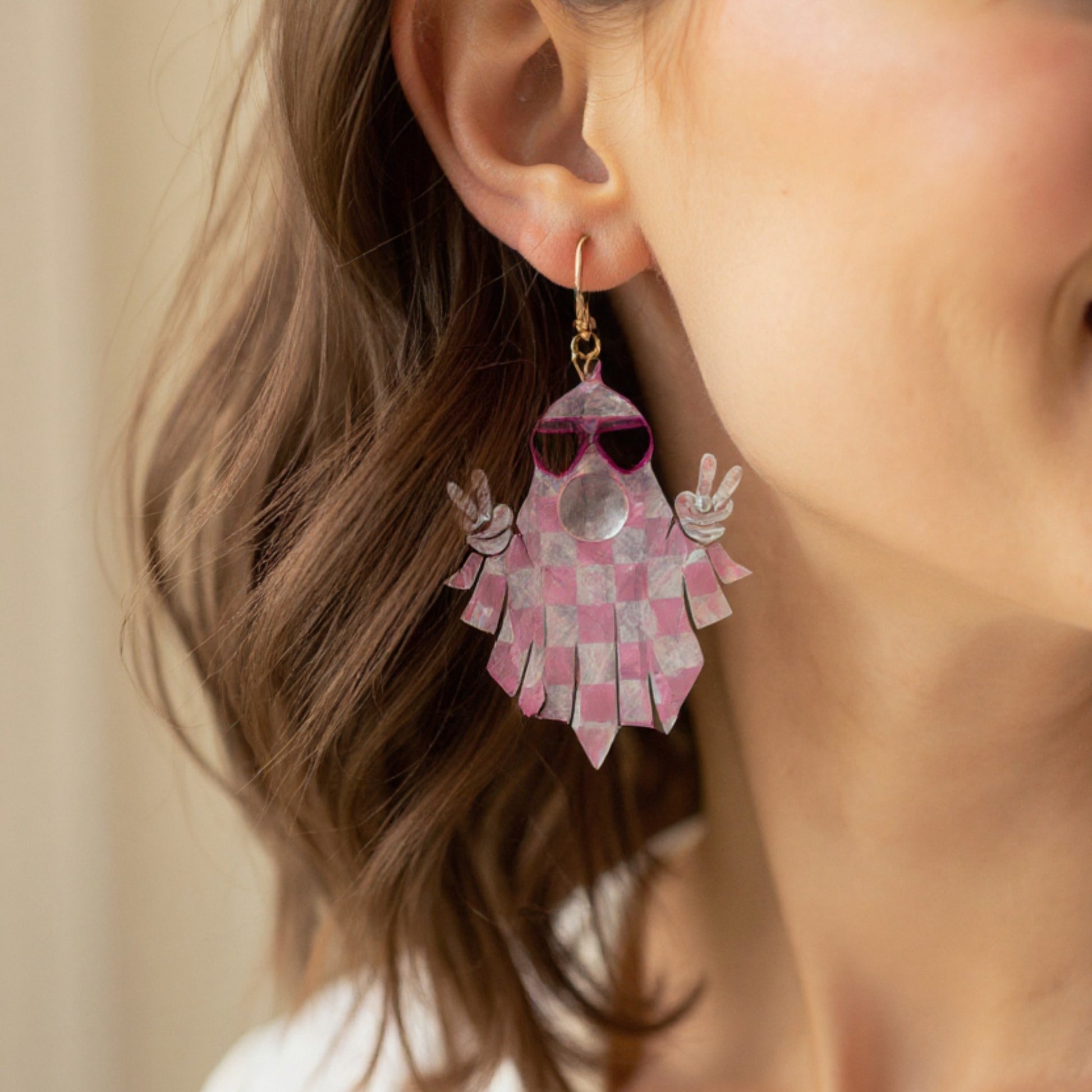 Close-up of a person wearing a unique pink and white checkered earring with sunglasses design.
