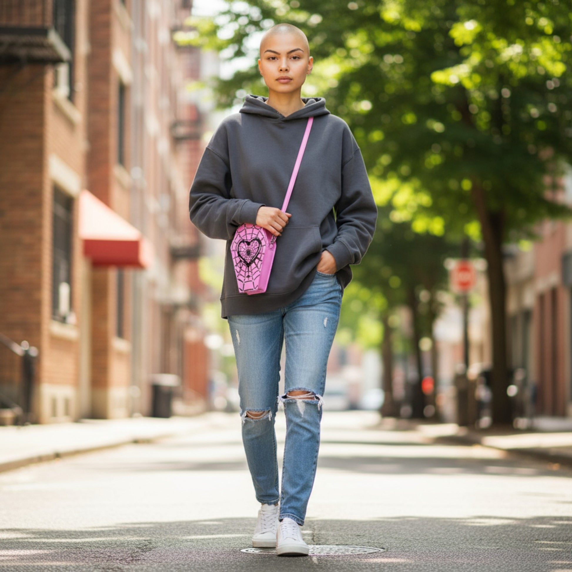 Person wearing a gray hoodie and ripped jeans with a pink bag on a city street.